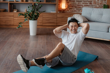 Happy asian man doing abs exercises, working out at home on fitness mat, full length portrait
