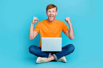 Full length photo of charming lucky man wear orange t-shirt rising fists winning modern device isolated teal color background