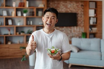 Fitness nutrition. Happy asian mature man holding bowl with fresh vegetable salad and showing thumb...