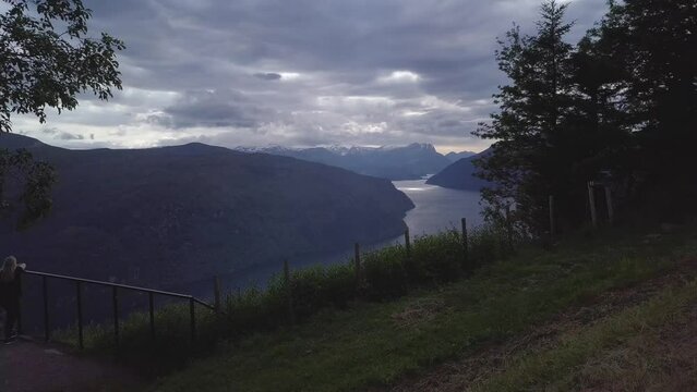 Flight over the Nordfjord Panorama viewpoint. To the side, the girl is standing with her back. In the background, the fjord and the mountains.
