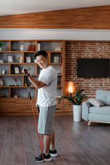 Athletic asian mature man working out with resistance band at home in living room interior,...