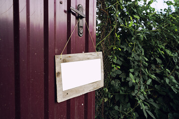Wooden signboard with white place for mockup hanging on door handle of countryside house outdoor