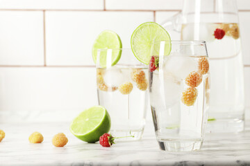 Glass and jug with fresh water and lime on marble table. Space for text. Flavored water. Summer drinks. Raspberry, mint and lime.