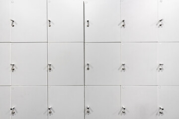 Large gray locker with each locker closed located beside corridors inside building are dimly lit.