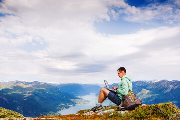 Naklejka na ściany i meble Young man sitting on the cliff using laptop