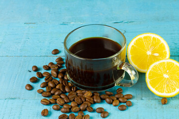 Black coffee in transparent glass with fresh lemon and coffee bean on blue wooden background. Espresso romano drink for healthy.