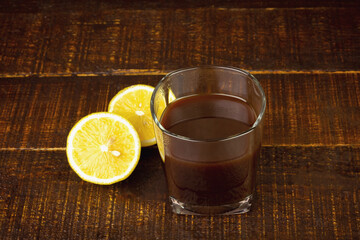 Black coffee in transparent glass with fresh lemon on brown wooden background. Espresso romano drink for healthy.