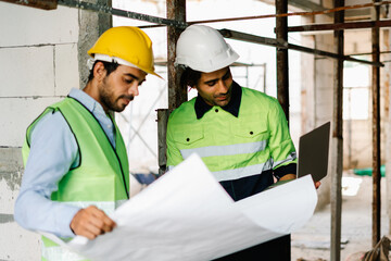 On building site, Two Construction Engineer in vest with wear safety hard hat looking at blueprint and laptop computer