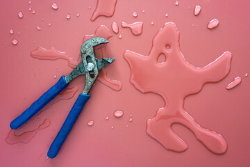 Wrench for plumbing lies on a pink background and spilled clean water. Copy space. Top view. 