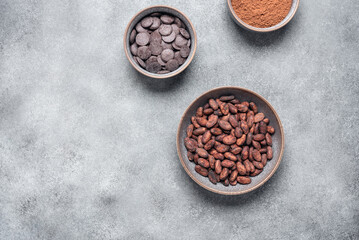 Chocolate, cocoa beans and cocoa powder in a bowl on a gray concrete background. Top view, copy space.