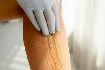 Cosmetologist depilates young woman's legs in spa center