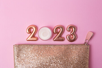 Top view of rose gold numbers 2023 and face cream from above,golden cosmetic bag near it.Good for...