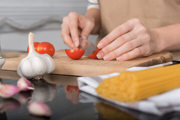 Women's hands cut a tomato on the kitchen table.