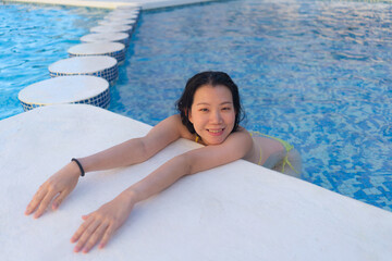summer holidays natural portrait of young happy and attractive Asian Korean woman enjoying relaxed and cheerful in swimming pool at hotel resort in tourism travel concept