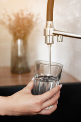 Woman filling drinking glass with tap water on the kitchen. Concept of clean drinking tap water at...