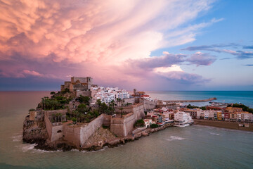 Fotografía aérea de la ciudad amurallada de Peñíscola al atardecer con nubes de colores en el...