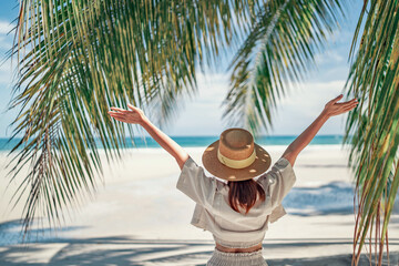 Summer beach vacation concept, Happy woman with hat relaxing at the seaside and looking away, in the summer against a backdrop of palm trees and sea beach.