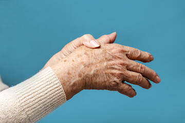 A senior woman is doing a brush massage, experiencing pain. Blue background, hands close-up. The...