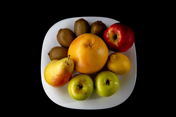 a plate of fruit. apple, grapefruit, pear, lemon, kiwi. dark background
