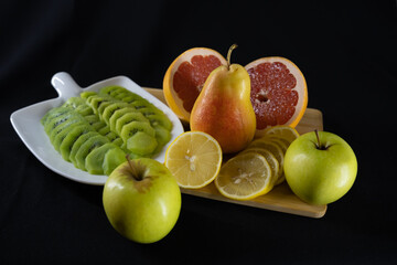 a set of fruits. kiwi slices. lemon, grapefruit, apples, pear. wooden board. dark background