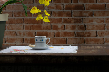 cup of coffee with orchid on wooden table. set table with a handmade crochet, hand embroidery butterfly and flowers. Brick wall background.