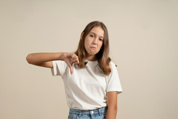 Young brunette woman in white t-shirt looking unhappy and angry showing rejection and negative with thumbs down gesture. bad expression