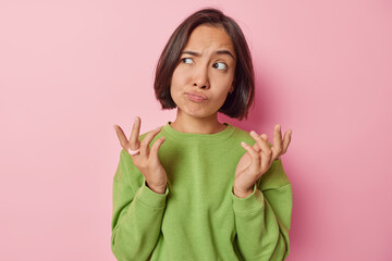 Clueless puzzled Asian woman shrugs shoulders feels hesitant about something spreads hands sideways...