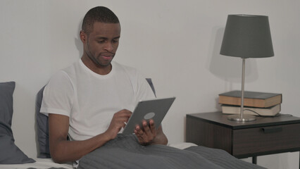 Man using Tablet while Sitting in Bed