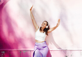 A young happy woman dressed in a white top and purple skirt, headphones, listening to music,...