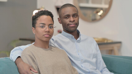 Portrait of Couple Looking at Camera While Sitting on Sofa, Side Pose