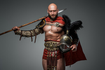 Shot of antique roman warrior with muscular build holding helmet and spear.