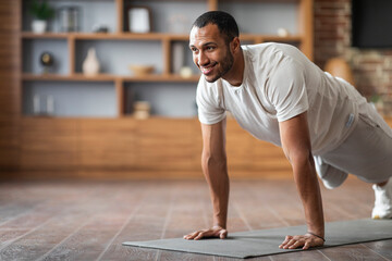 Fototapeta na wymiar Active Sporty Black Male Training At Home, Making Plank Exercise