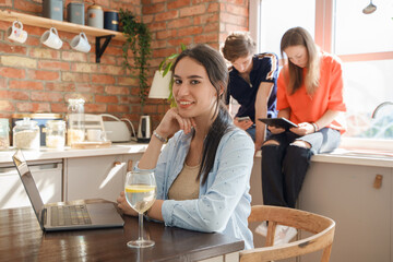 Portrait of young woman sitting at table with laptop and her two friends using tablet.