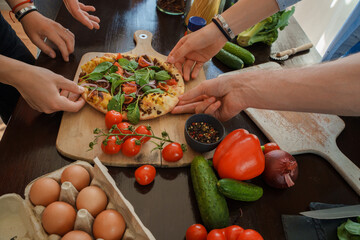 Shot of four friends taking their own pieces of pizza and celebrating event together at home.