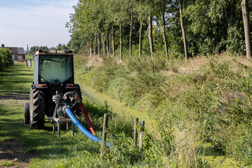 Small tractor with water pump pumps water from ditch for spraying the fruit trees in the Betuwe in...