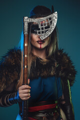 Portrait of ancient valkyrie with fur coat hiding her face with hatchet and looking at camera.