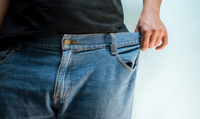 Man wearing and stretching his blue jeans because the pants are too big for him on blue background