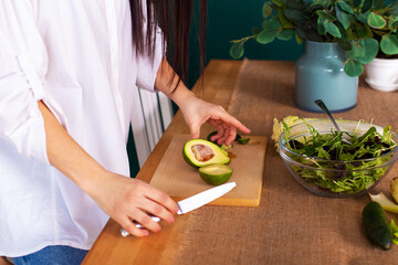 young woman prepares salad in the kitchen, cuts avocado. hands close up