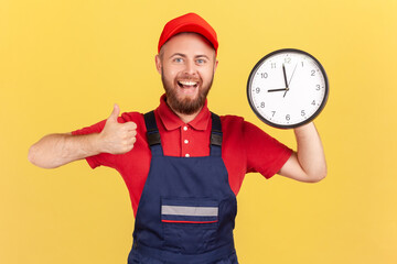 Portrait of happy smiling handyman standing with big wall clock in his hands, looking at camera and...