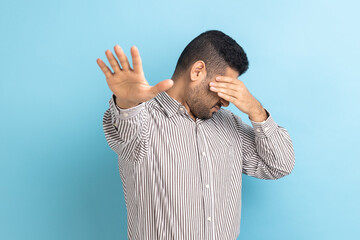 Scared confused businessman with beard closing eyes with palm of hand, stretching out another hand...