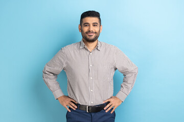 Portrait of happy attractive bearded businessman with smile holding hands on hips, looking at...