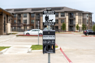Dog waster station sign with plastic bags for waste. Clean after your dog while walking in residential complex, waste station with baggies with building and car parking on background.