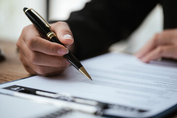 Close up of business's hand signing on agreement paperwork for selling and loan financial house...
