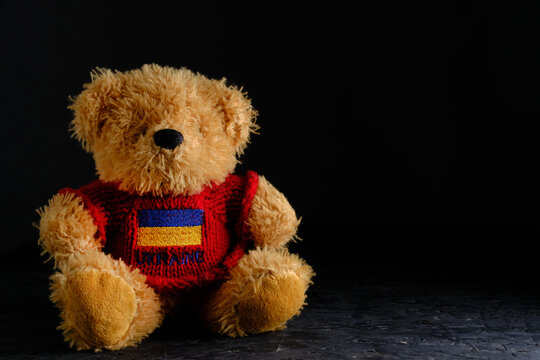 Soft toy on a black background, bear red jacket with flag Ukraine depicted on it.