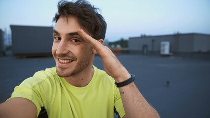 Smiling sportsman looking at camera and gesturing on roof in evening.