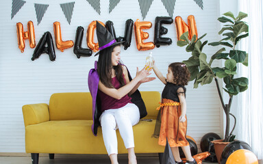 Asian beautiful woman or mother and little Caucasian sweet girl wearing witch costume with hats, playing trick or treat with fun, smiling with happiness, celebrating Halloween party at home.