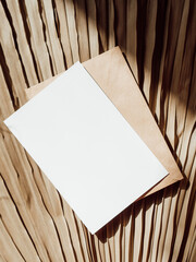 Blank white card, envelope on beige dry palm leaf background top view.