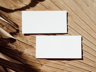 Two white business cards branding mockup template on beige dry palm leaf background top view