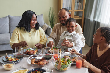 African family of four having holiday dinner together at table at home, they eating and talking