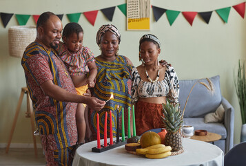 African family of four burning candles together to celebrate Kwanzaa holiday together at home